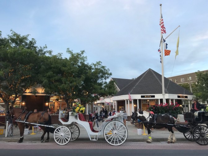 Two horse-drawn carriages in front of shopping plaza.