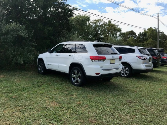 Jeep parked on field in row of cars and SUVS.
