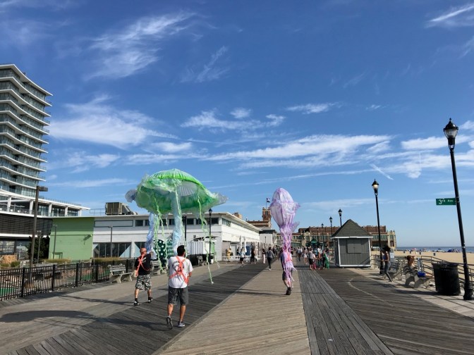 Men carrying large jellyfish parade decorations along Asbury Park boardwalk.