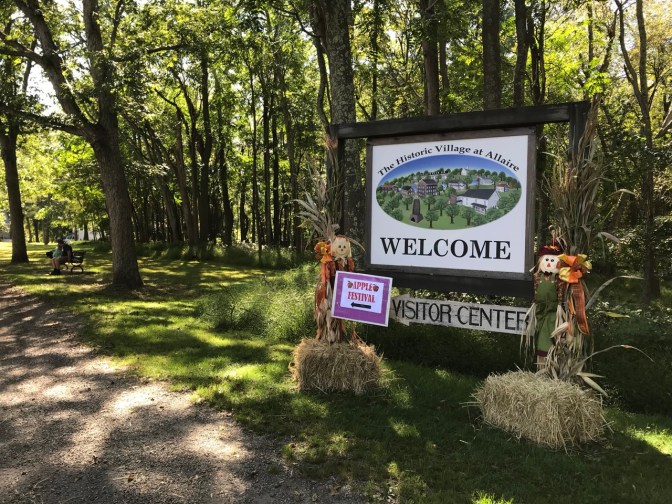 Entrance sign that says THE HISTORIC VILLAGE AT ALLAIRE WELCOME VISITOR CENTER, surrounded by straw bales and fall decorations.