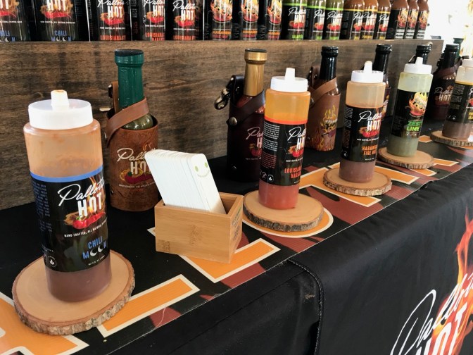 Row of hot sauce bottles to taste, with glass bottles of hot sauce in rows behind.