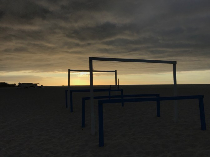 Tent frames on beach, with sunrise breaking through clouds.