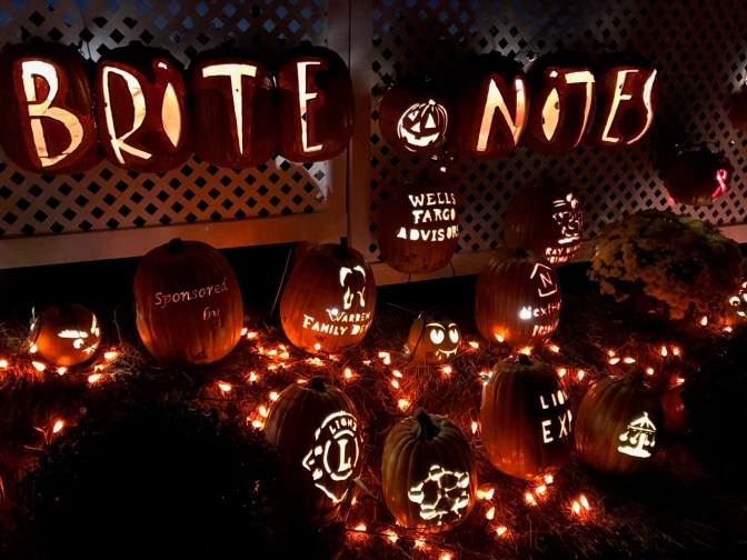 Stand of Pumpkins with sign carved into pumpkins saying BRITE NITES and logos for sponsors carved into other pumpkins.