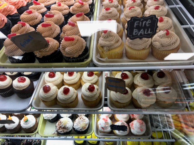 Shelves full of cupcakes with signs for FIREBALL KAHLUA CAPPUCCINO, and others.