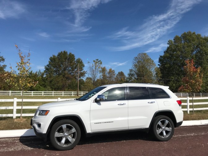 White 2014 Jeep Grand Cherokee, parked in front of a white picket fence.