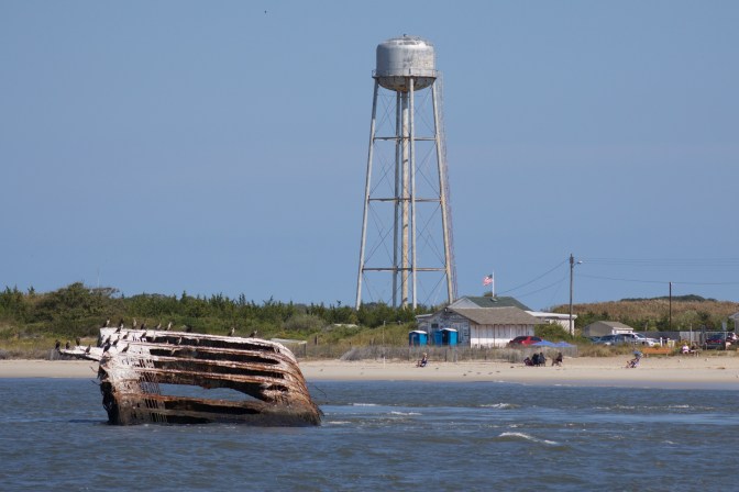 SS Atlantus wreckage in the ocean, with a water tower on the beach in the background.