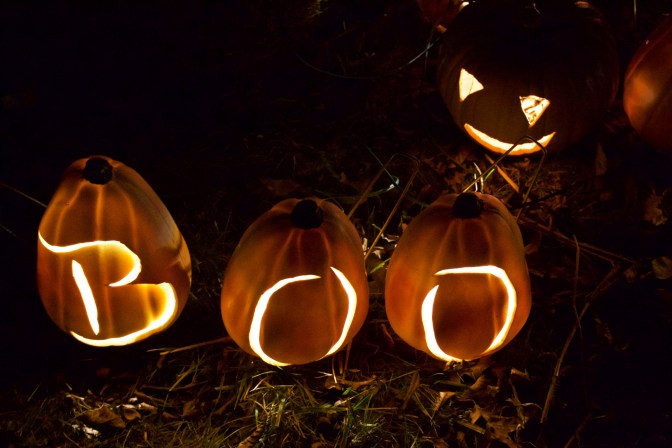 Three pumpkins, carved BOO with a traditional jack-o'-lantern in the background.