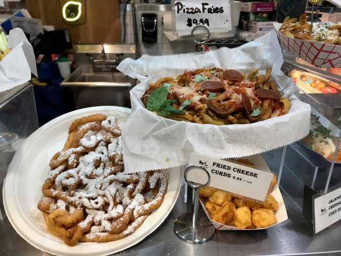 Plates with pizza fries, fried cheese curds, and funnel cake.