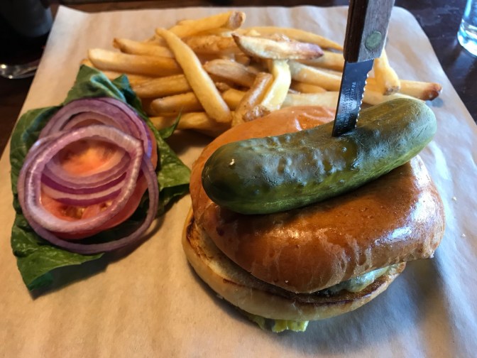 Cheeseburger, pickle, fries, and topping, served on a butcher block.