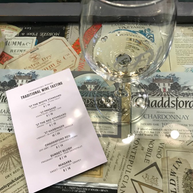 Wine glass and wine tasting card on bar top covered with wine labels.