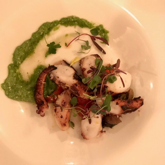 Charred octopus with garlic scale pesto on a white plate.