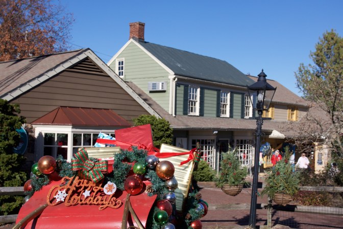 Red sleigh filled with presents in foreground, with shops in background.