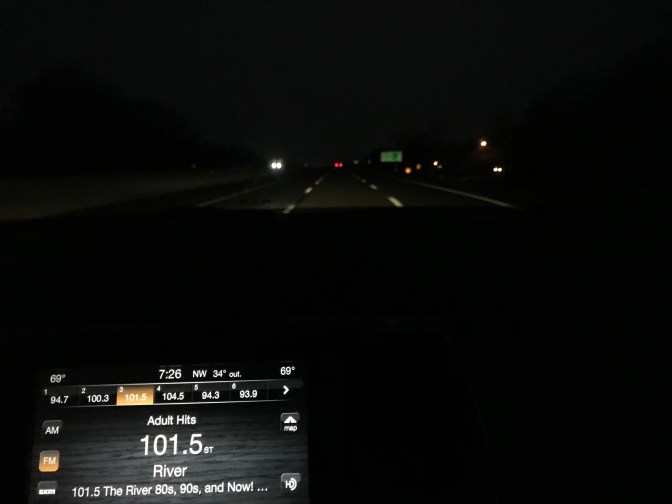 View of road in darkness behind car dashboard. Clock on dashboard reads 7:26 am.