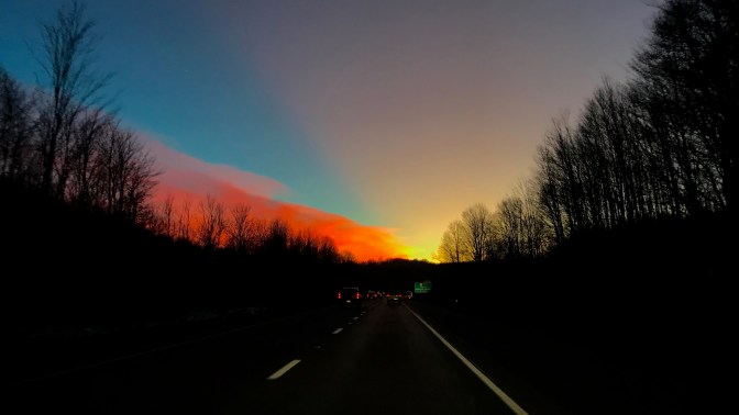 Sunset sky over I-80 with trees on either side of road.