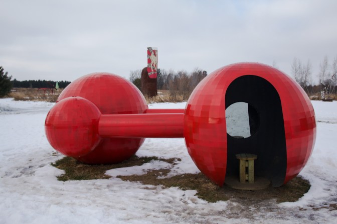 Metal sculpture with two large spheres and two smaller spheres, connected by pipes.