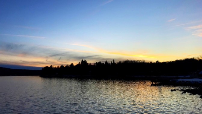 Sunset sky with tree-lined lake view.