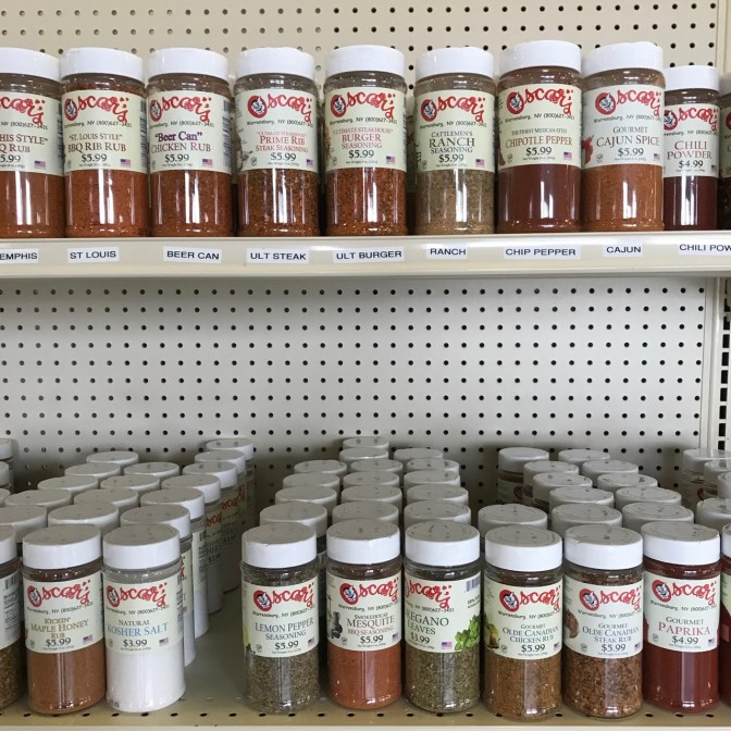 Two shelves of bottles of spices, including burger seasoning, kosher salt, chili powder, cajun spice, chipotle pepper, and others.