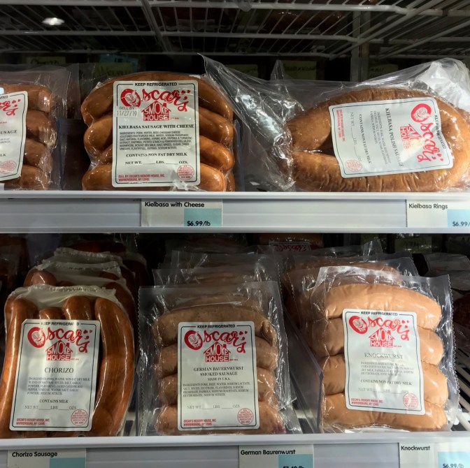 Packages on refrigerator shelves with chorizo, kielbasa, bratwurst, knockwurst, and other sausages.