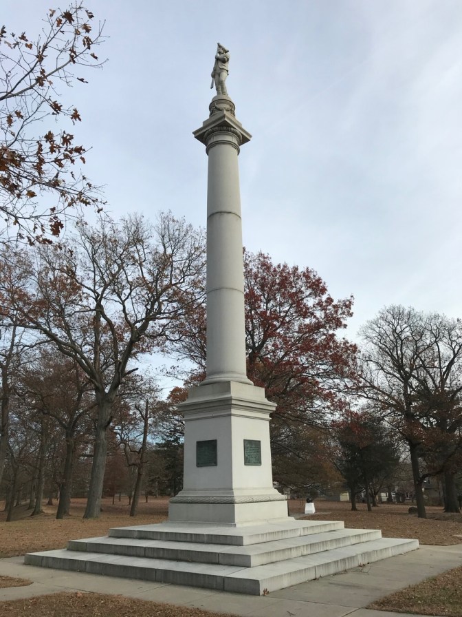 Tall monument of soldier on pedestal, in white marble.