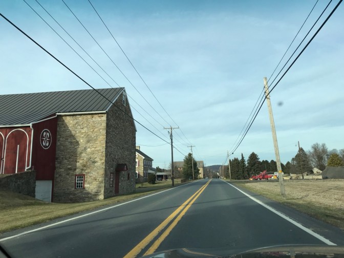 Two-lane country road with barns on either side of road.