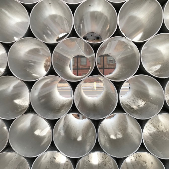 Series of metal tubes arranged in a honeycomb sculpture.