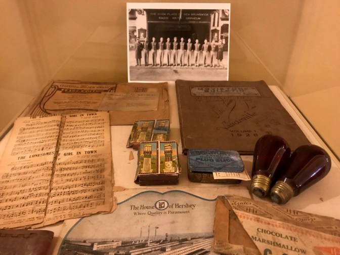 Glass display case with objects from the theater's history including play bills, match boxes, pictures, and music.