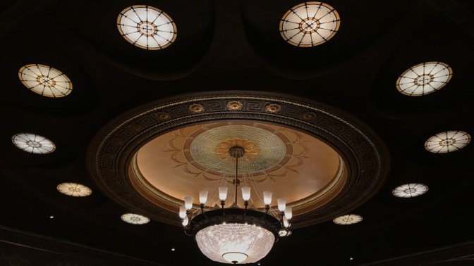 Chandelier hanging from ceiling surrounded by twelve skylights.