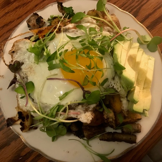 Plate of avocado, sausage, egg, greens.