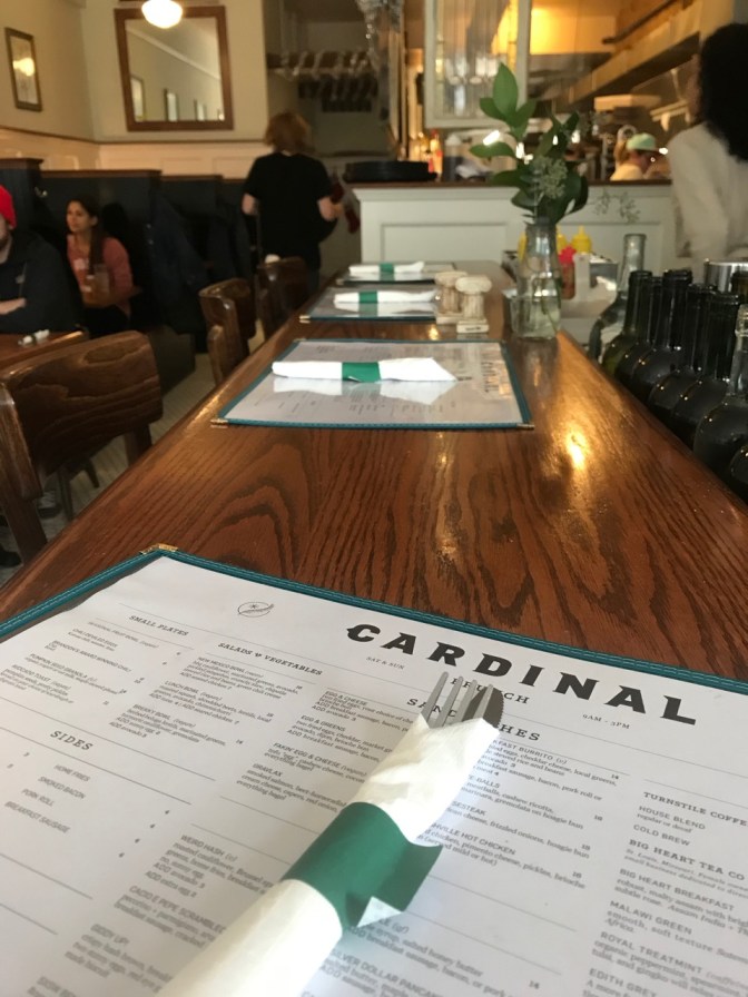 Menu and countertop of bar at Cardinal restaurant. Booths and open air kitchen are in the background.