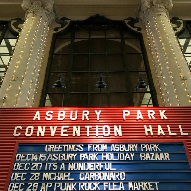 Billboard inside convention center that says ASBURY PARK CONVENTION HALL GREETINGS FROM ASBURY PARK DEC 14 15 ASBURY PARK HOLIDAY BAZAAR.