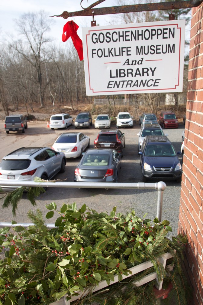 Sign hanging from building that reads GOSCHENHOPPEN FOLKLIFE MUSEUM AND LIBRARY ENTRANCE. In background is a parking lot with several cars, including 2012 Honda Accord coupe.