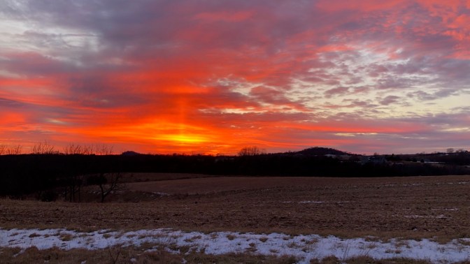 Sunset over rural farmland with hills in the distance.