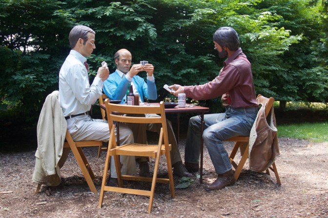 Statue of three men playing cards around card table, with a fourth chair empty.