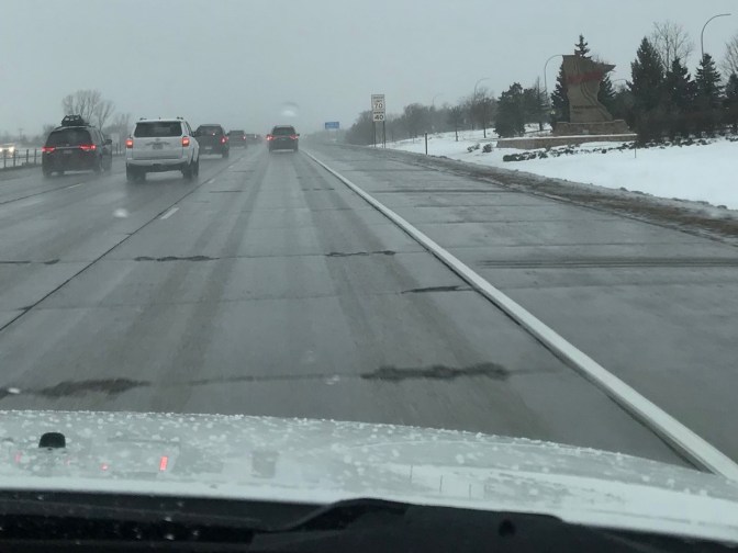 Wet and snowy road with welcome sign for Minnesota on right.