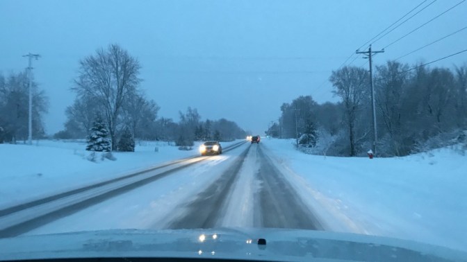 Snow-covered road with tire tracks through the snow.