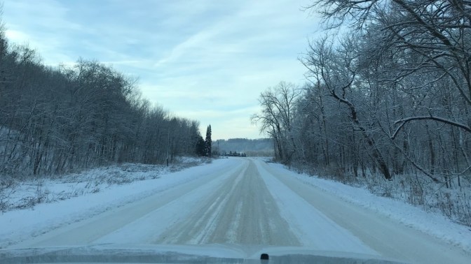 Snow-and-ice covered road with snow-covered trees along the side of the road.