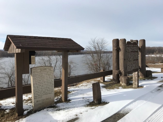 Two roadside historical markers, one in stone, the other in wood.