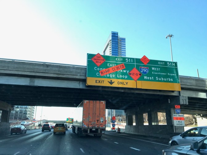 Road sign on overpass that says EXIT 511 EAST CHICAGO PKWY CHICAGO LOOP with red signs indicating exit closed.