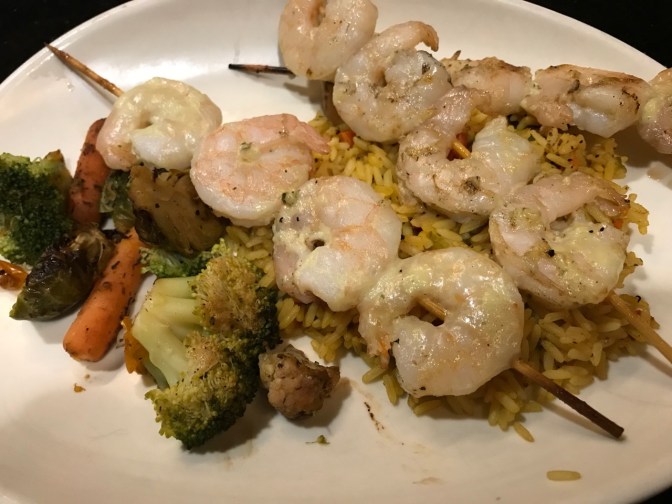 Shrimp on skewers with rice and mixed vegetables, on white plate.