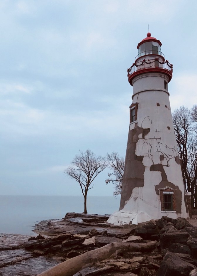 Exterior of Marblehead Lighthouse, a white and gray lighthouse on a rock shoreline.