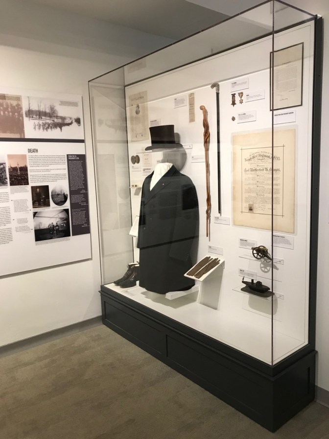 Glass display case with black coat, top hat, gloves, cane, and other personal effects of Rutherford B. Hayes.