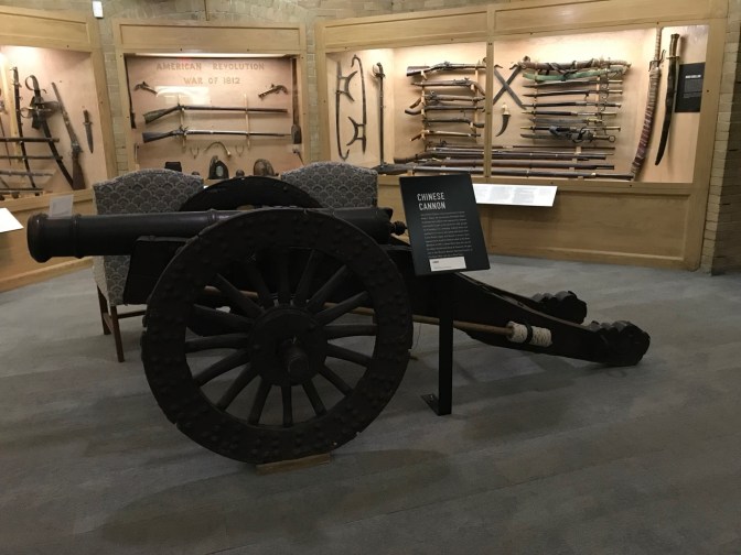 Large Chinese cannon in room filled with guns and swords.
