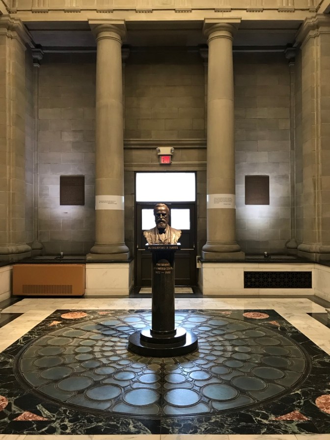 Stone and marble atrium, with bust of President Hayes in middle of room.