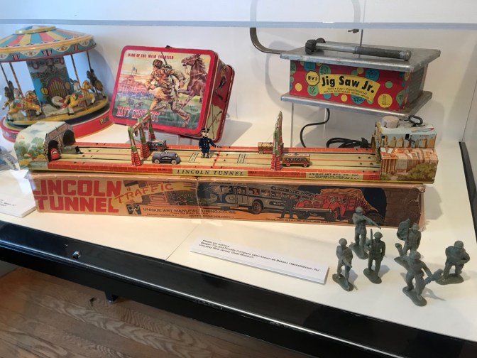 Display of 1950's toys including Lincoln Tunnel model car toy, a luncbox, a carousel, and a toy jig saw.