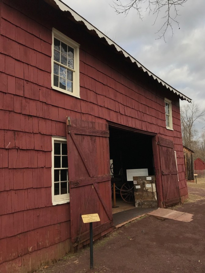 Exterior of blacksmith shop, painted red, with white window trim.