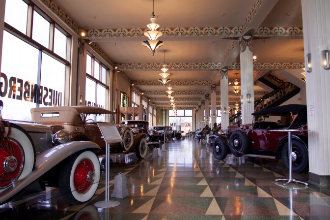Showroom of old Duesenberg car dealership with classic cars on floor.