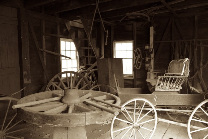 Wooden wheel being constructed in wheelwright shop, and a carriage is in the background.