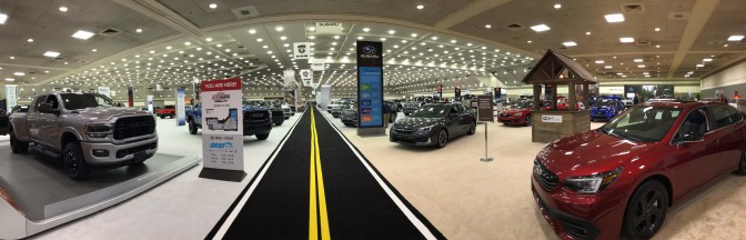 Panorama of interior of auto show, with the main pedestrian thoroughfare painted to look like a two-lane road.