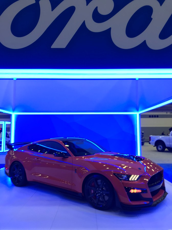 Red Ford Mustang coupe under blue awning.