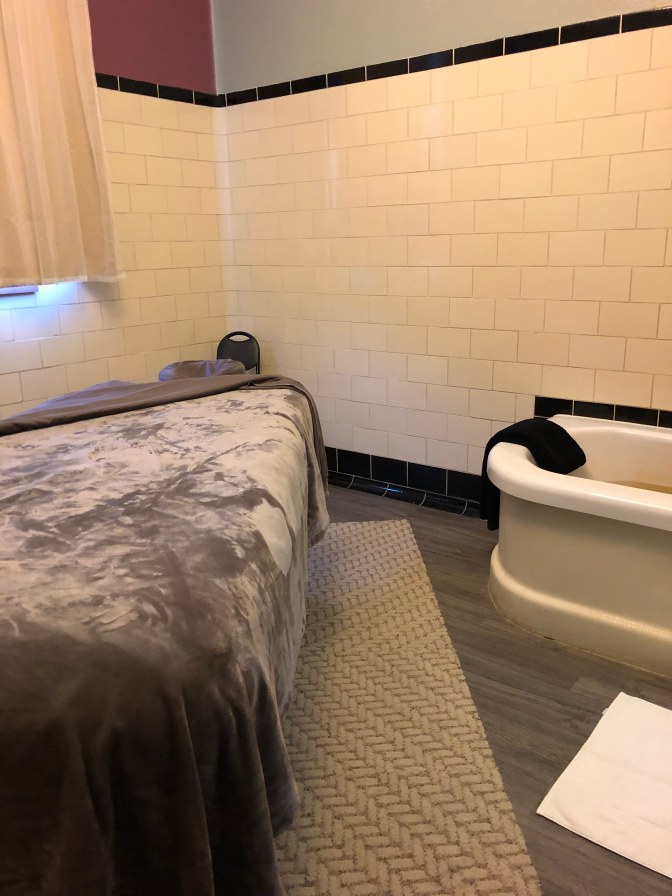Bathtub with mineral water and massage table in tile-covered room.